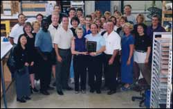 Senator Paul Wellstone (D--MN) and his wife, Sheila, hold a plaque presented by TEC Interface Systems as they pose with the TEC staff. Flanking them are TEC President Scott Schneider (right) and CEO Carl Caspers, CPO (left). Standing next to him is his wife, Barb. Senator Wellstone visited TEC to announce the new custom K-Codes.