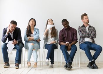 Diverse casual work candidates get bored while sitting in queue for job interview, multiethnic applicants holding smartphones, tablets and resumes tired of waiting. Concept of hiring, employment, HR