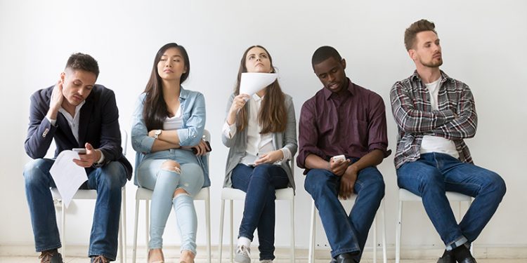 Diverse casual work candidates get bored while sitting in queue for job interview, multiethnic applicants holding smartphones, tablets and resumes tired of waiting. Concept of hiring, employment, HR