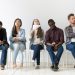 Diverse casual work candidates get bored while sitting in queue for job interview, multiethnic applicants holding smartphones, tablets and resumes tired of waiting. Concept of hiring, employment, HR
