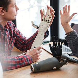 Compare it with my hand. Close up portrait of the male engineer looking attentively at the prosthesis hand and comparing it with real hand while working at the table with his colleague. Stock photo